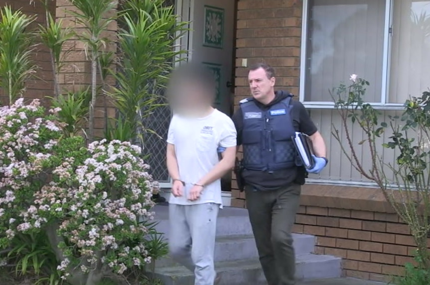 A handcuffed youth is led away from a home in Melbourne's south-east by a police officer.