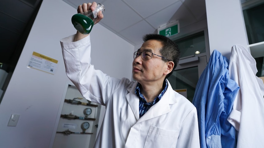A professor holds a glass beaker in the air and looks at the base of it from underneath