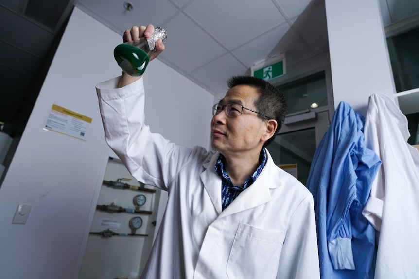 A professor holds a glass beaker in the air and looks at the base of it from underneath