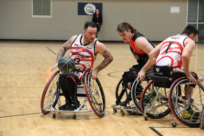 A dark-haired man with tattooed arms faces off with an opponent during a wheelchair basketball game.