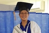 Jenny Han dressed in hospital scrubs, holding a rolled parchment and wearing a graduation mortar board.