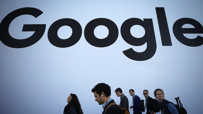 People walk in front of a black Google logo.