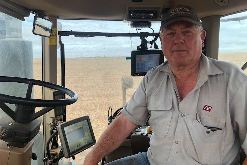 A farmer sits inside the cabin of his tractor. Outside the windows you can see dry paddock