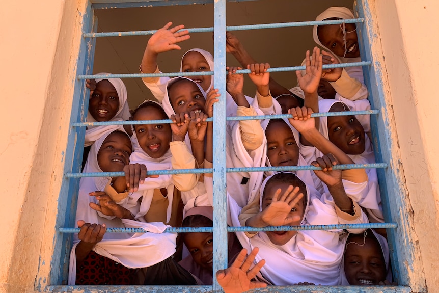 Smiling girls waving through the bars of a window.