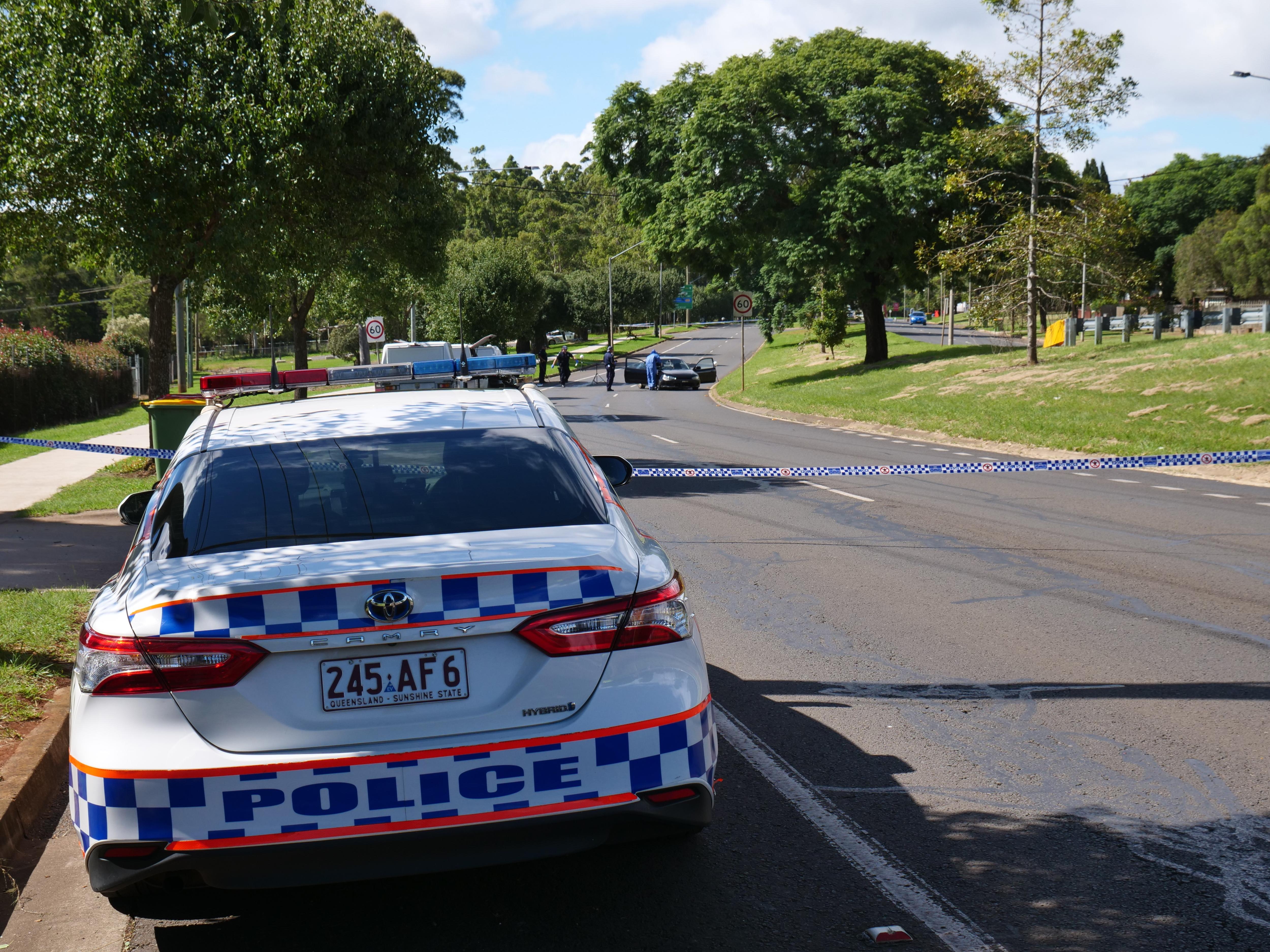 A police car parked on the left hand side of the road with police tape across the road