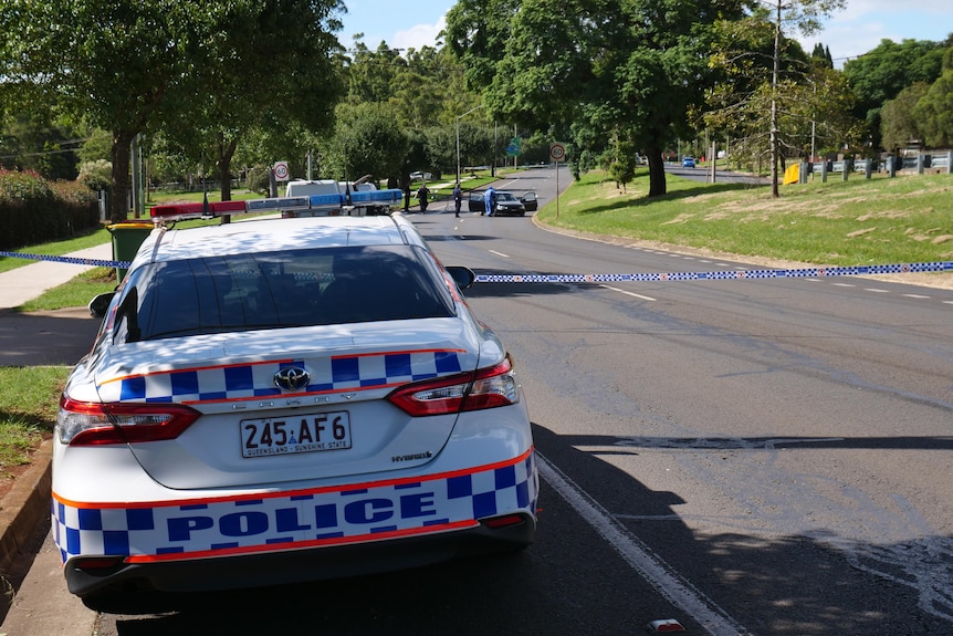 A police car parked on the left hand side of the road with police tape across the road