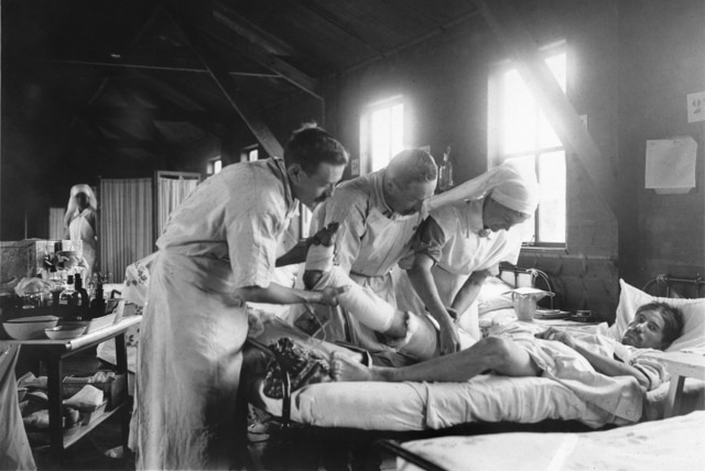 Two men and a nurse apply a dressing to the leg of a wounded French soldier, at a mobile hospital south-west of Amiens in WW1.