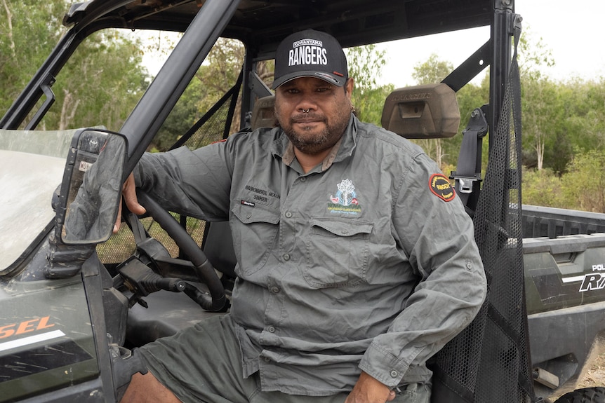 An Indigenous man sits at the wheel of an all-terrain buggy wearing a khaki rangers uniform.