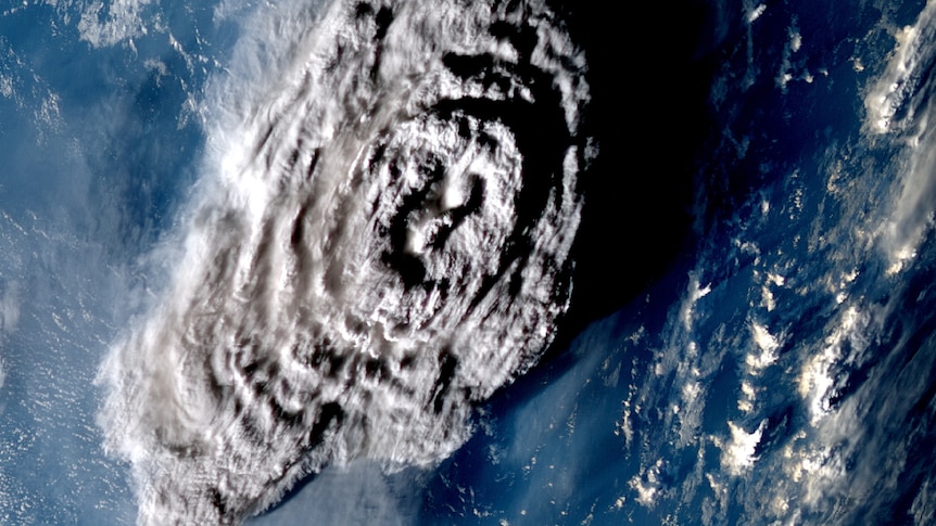 An areal shot of a large plume of gray ash over a blue ocean.