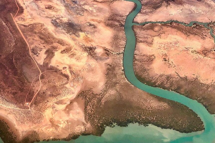 Aerial view of barren coast with a green creek winding through the red dirt and rock to the sea.