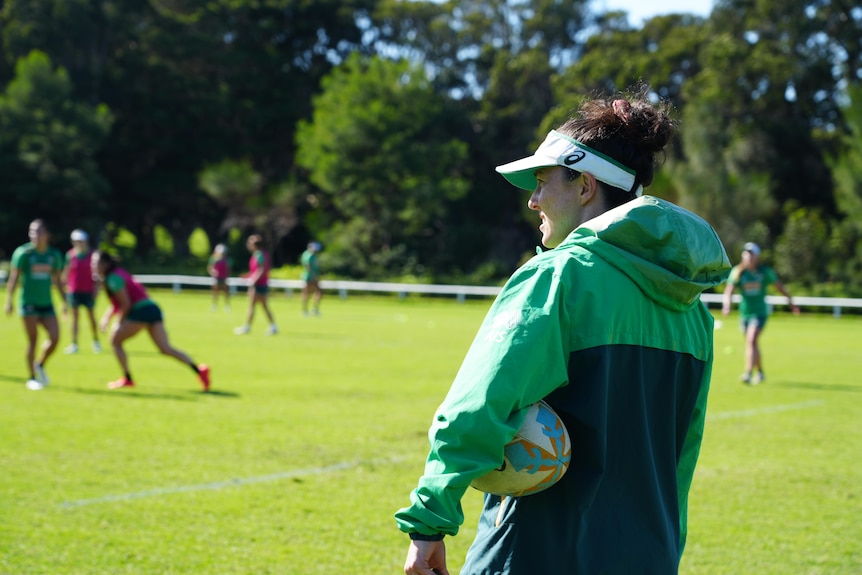 Australian women's rugby 7s assistant coach Emilee Barton holds a ball under her arm and watches training.