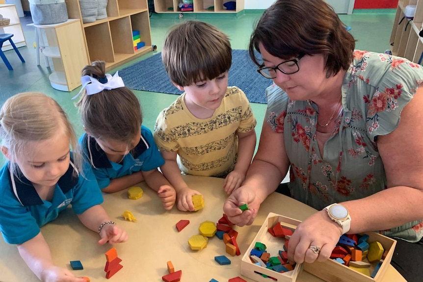 A woman kneels at a table with children.