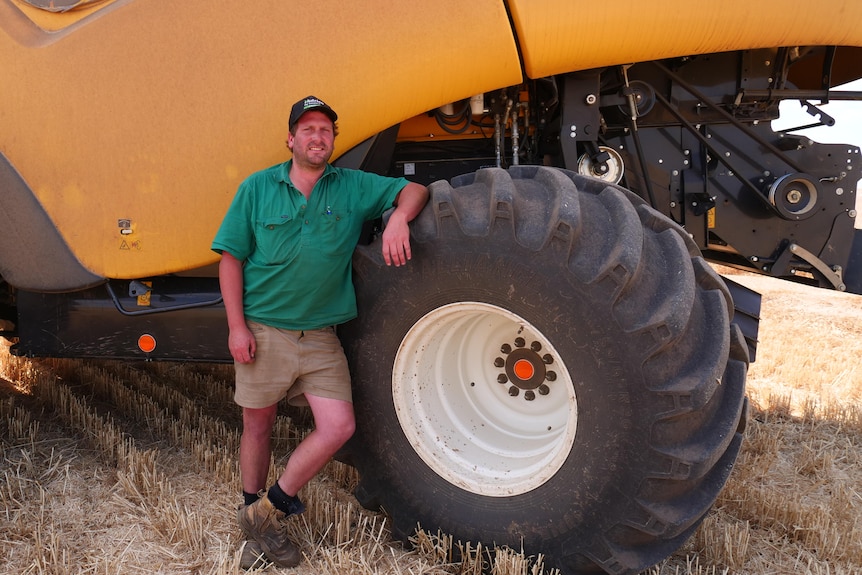 A farmer stands in front of a large yellow tractor
