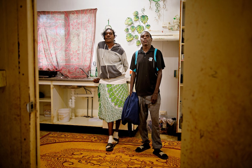 A man and a woman stand in an old house by a sink. 