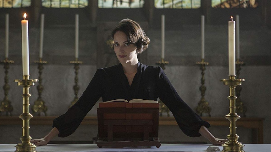 A young woman with cropped, brunette hair in a black dress, stands at an grand catholic church altar.