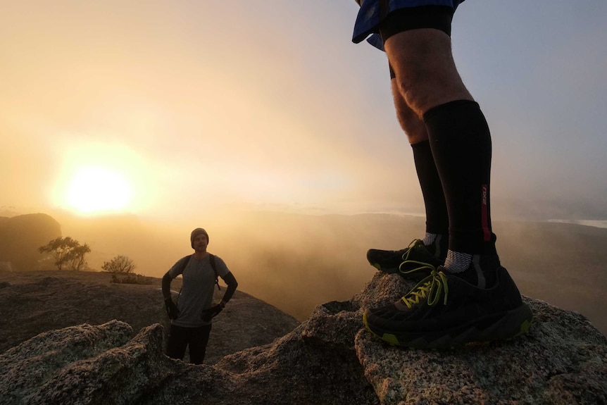 Two runners on top of large granite boulders a sunrise.