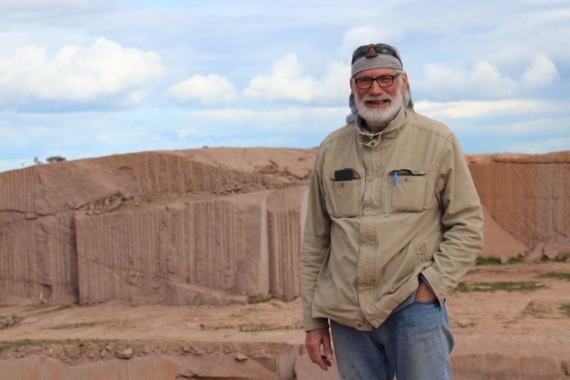 Man standing in foreground above pink granite quarry with walls of rock in far background