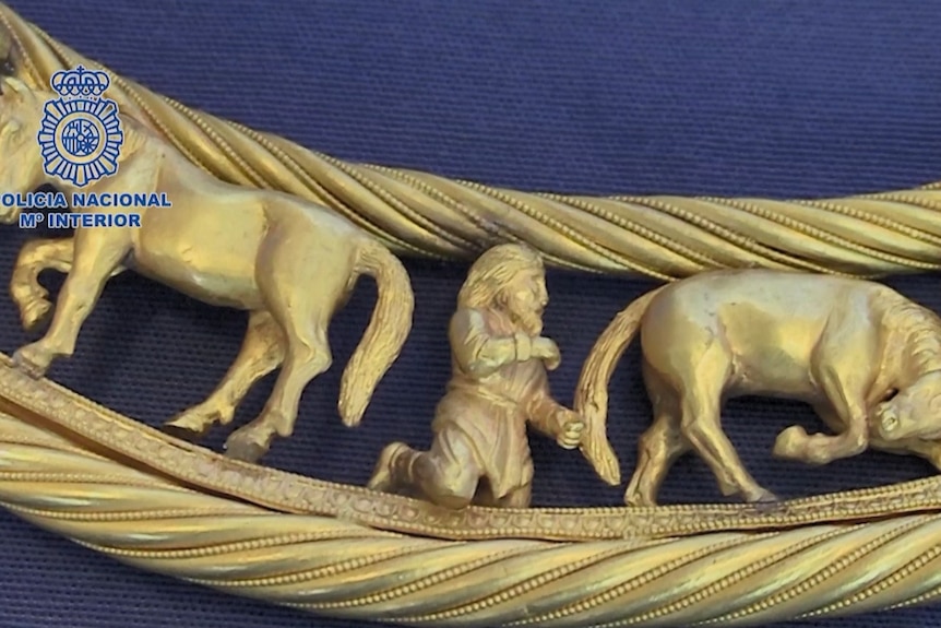 close up of a closed gold necklace showing men crouching next to horses 
