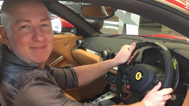 A bald man looks at the camera while sitting in a Ferrari.