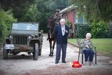 Three people and a horse and army vehicle stand on a driveway