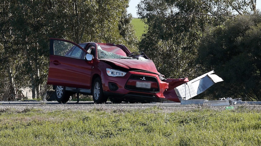 A maroon car with its left side destroyed and its roof and windscreen crushed inwards.