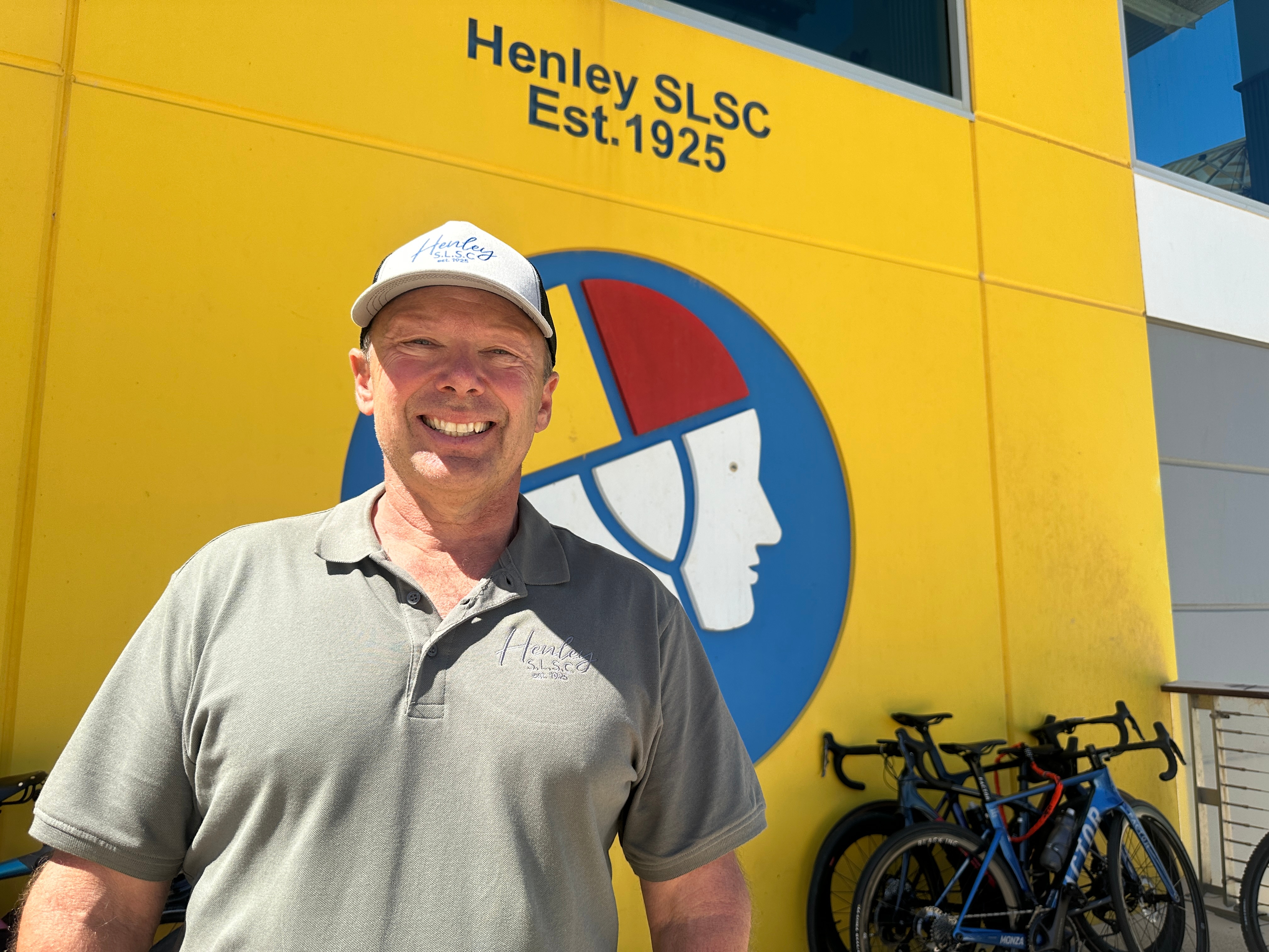Um homem vestindo uma camisa pólo verde em frente a um prédio amarelo com um desenho de salva-vidas de surf.