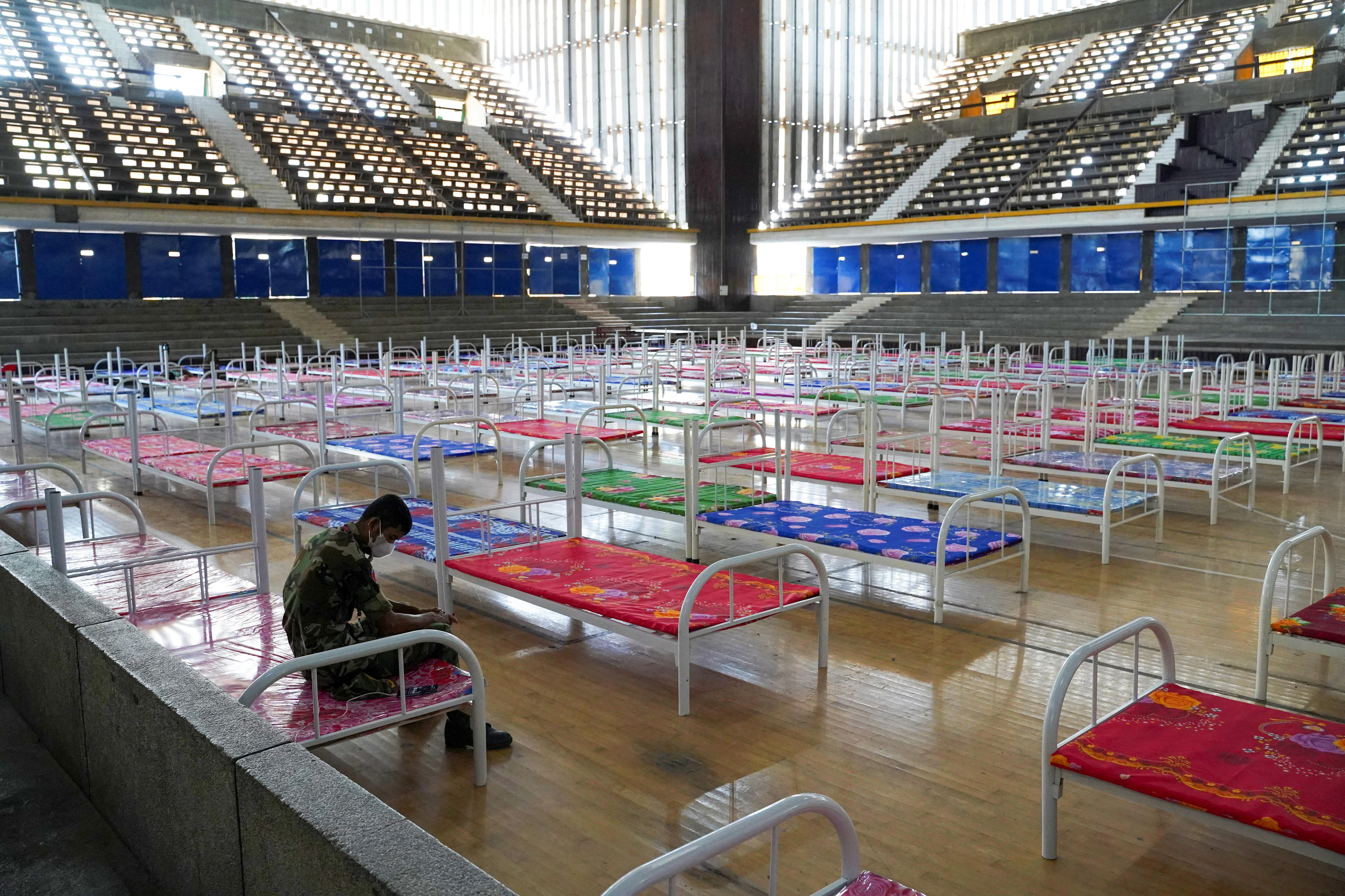 A man sits in a gymnasium, which has been filled with hospital beds 