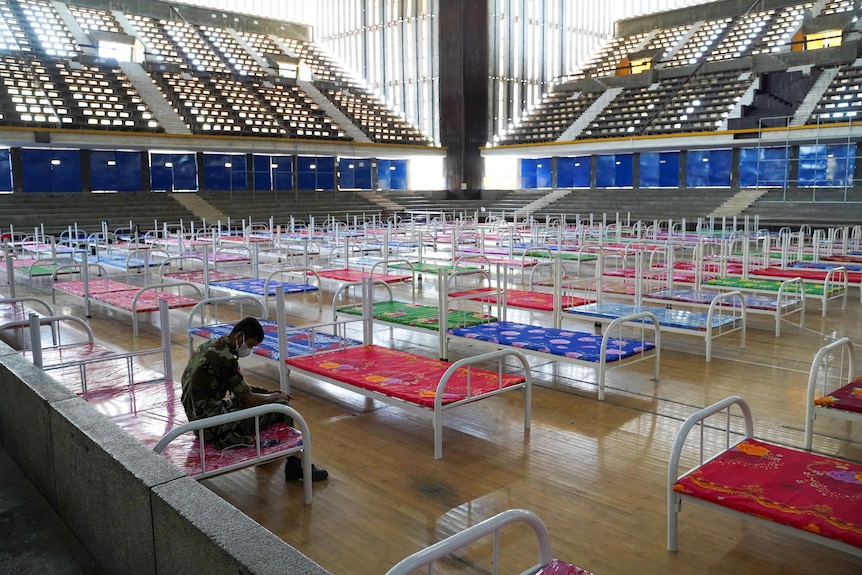 A man sits in a gymnasium, which has been filled with hospital beds 