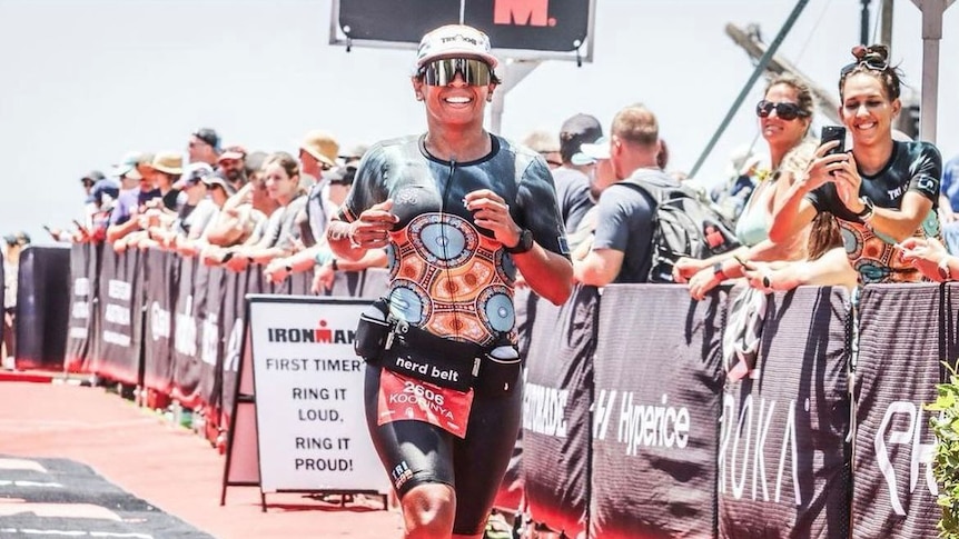 Female Indigenous athlete Koorinya Moreton running in Ironman competition while being cheered on by spectators.