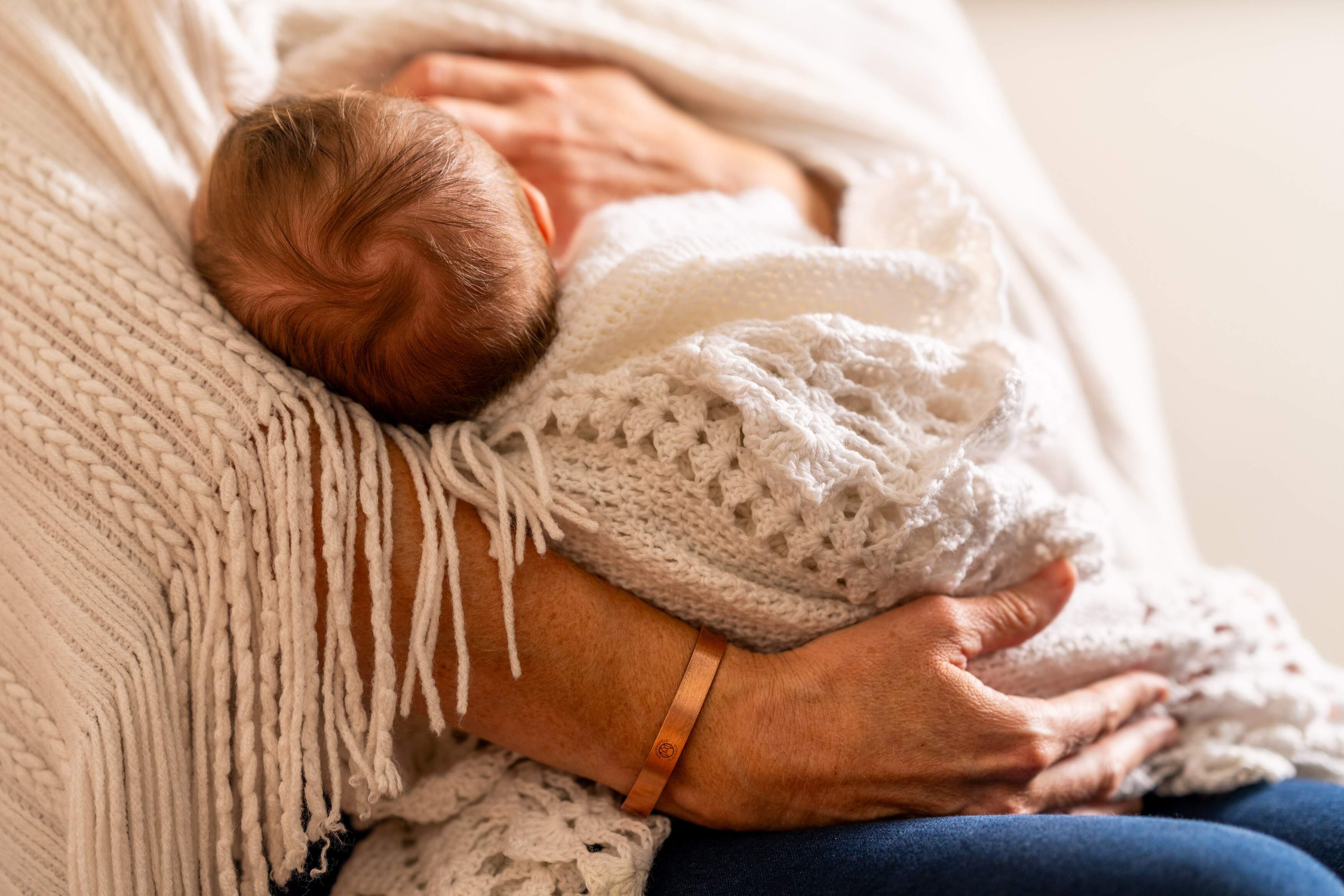Close up photo of a baby wrapped in white blankets being held by a woman, neither of whom are identifiable