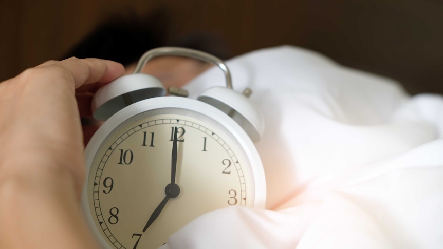 a hand picks up an old-fashioned alarm clock