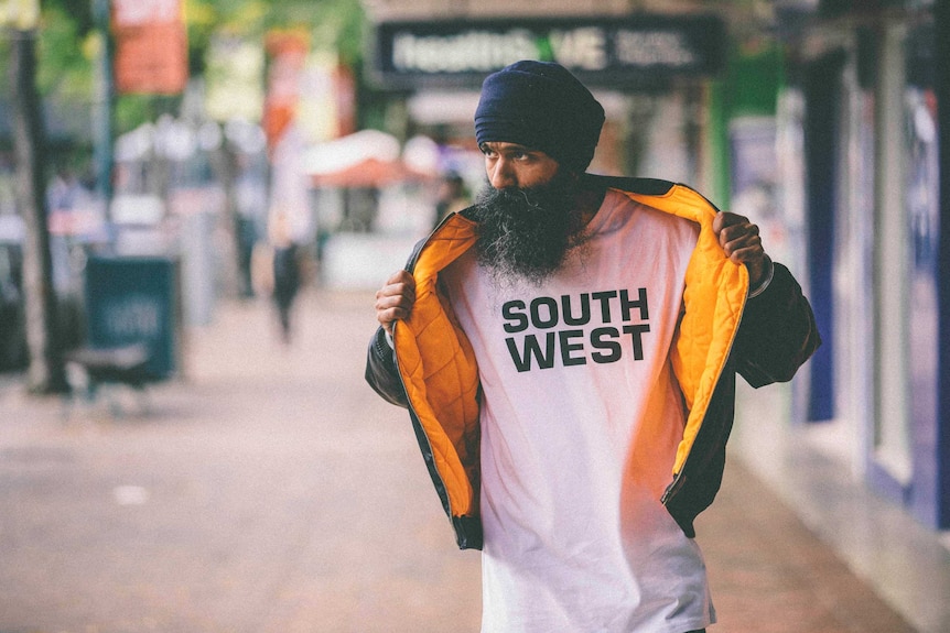 Rapper L-FRESH walking along street, opening his jacket to show a tee-shirt with the words 'South West'.