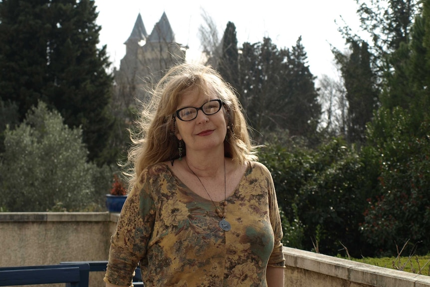 A woman standing with a French chateau and trees in the background.