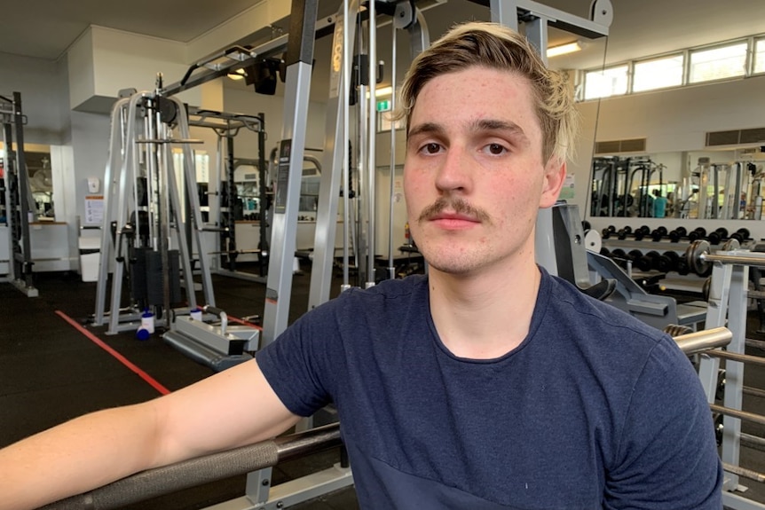 Young man sits on gym equipment in gymnasium.