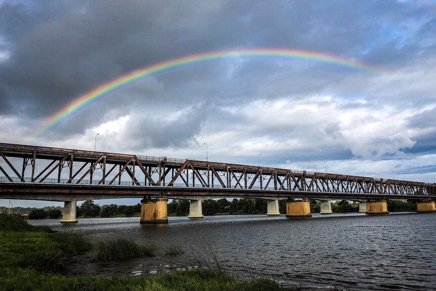 An iron bridge over a river with a rainbow overhead.