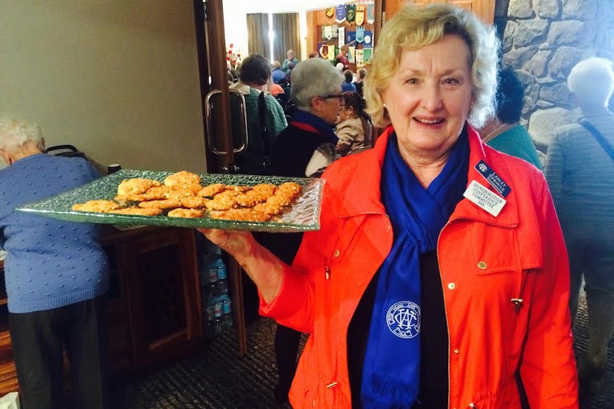 A woman holds out a tray of Anzac biscuits.
