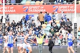 Fans are in focus, with North Melbourne and Geelong players blurry in the foreground during an AFL game in Hobart.