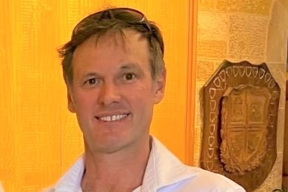 A man in a white shirt stands against a yellow wall