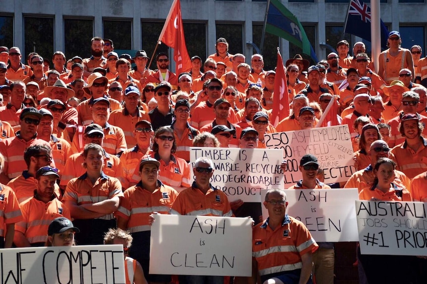 More than 100 workers rally in Melbourne, holding signs and flags.