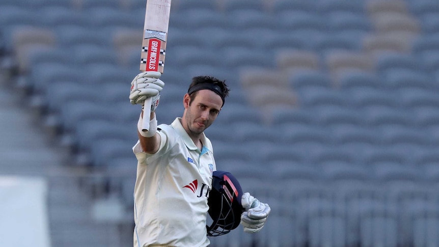 A headband-wearing cricketer raises his bat in salute after reaching a century.