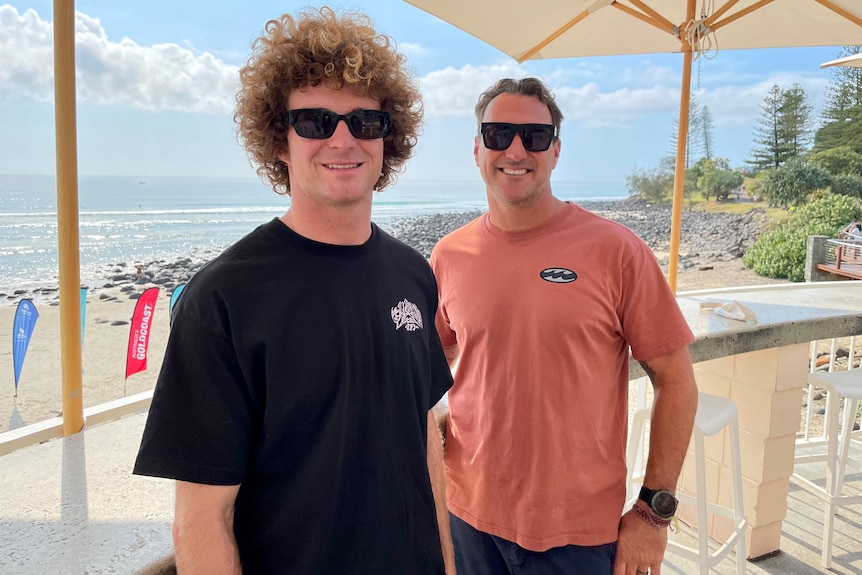 two pro surfers standing side by side with the ocean in the background