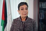 Hanan Ashrawi stands in front of two flags in an office