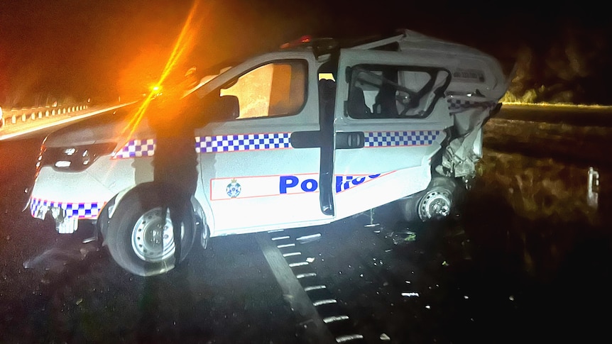 A smashed police car against a guard rail on a highway backlit by a spotlight