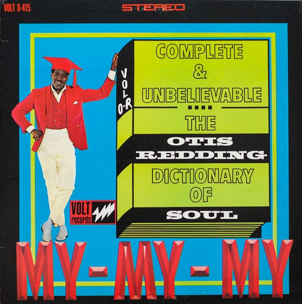 Otis Redding wears a red graduation cap and stands next to an oversized dictionary
