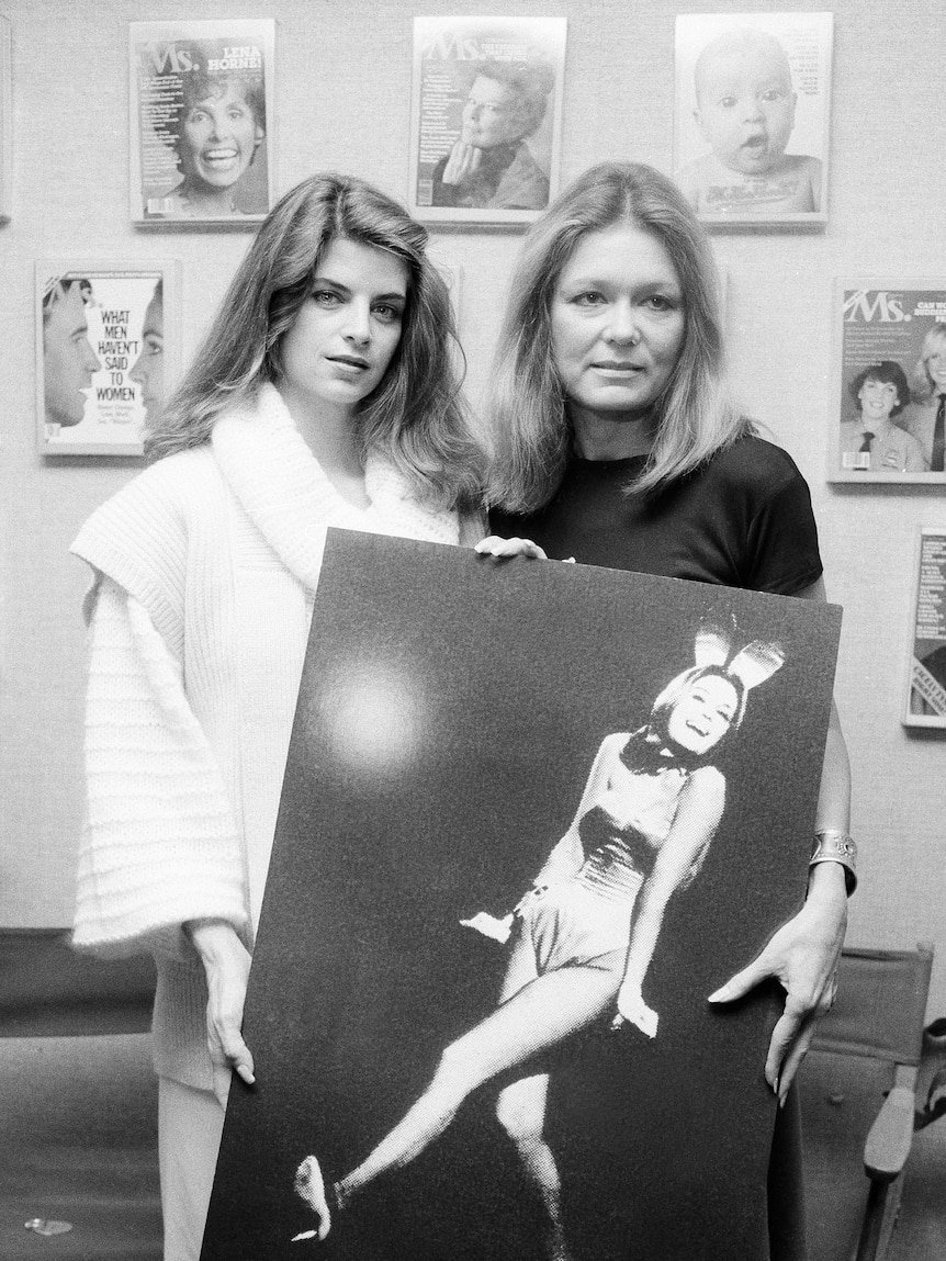 A black and white portrait of two women holding a poster.