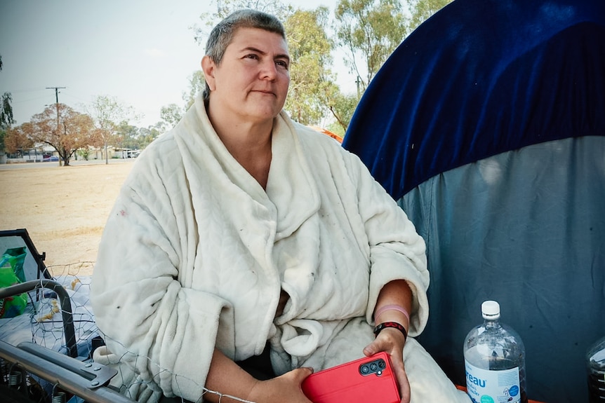 A woman sits in a dressing gown next to a tent.