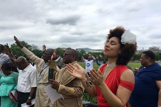 African-American woman Joy Villa wears a red dress and stands in a prayer circle near the white house.