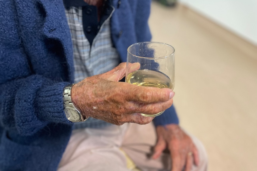 A close up shot of a man in a blue sweater holding a glass of alcohol