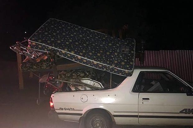 A sideview of a white ute overloaded with furniture at night.