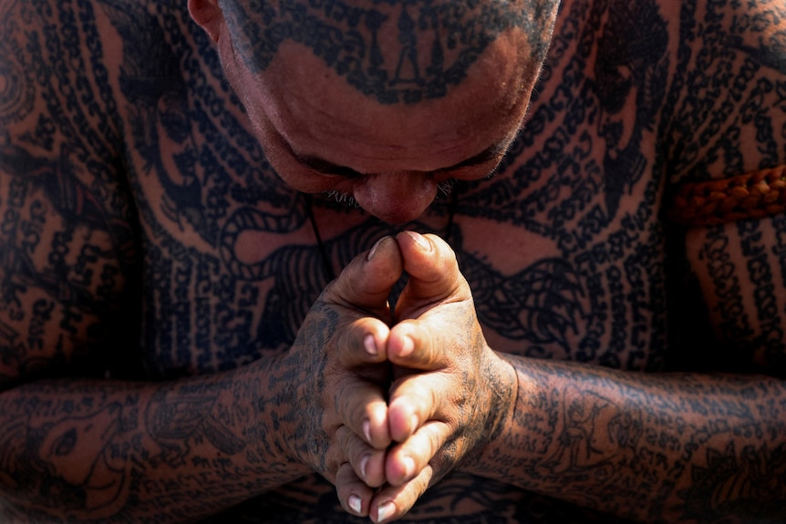 A devotee, who has green script tattoos across his body except for his face, prays at a religious tattoo festival